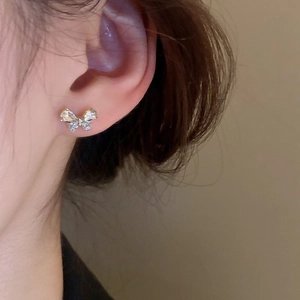 Close-up of a silver butterfly stud earring with diamonds worn on the ear for women