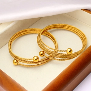 Dettaglio di due bracciali rigidi a cavo dorati con estremità a sfera in un cofanetto