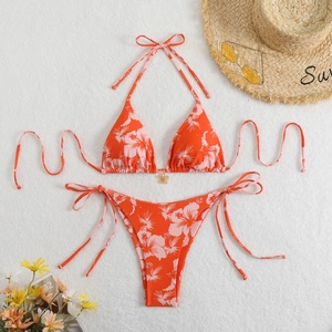 Flat lay of orange hibiscus print bikini set with gold flower pendant on white fur
