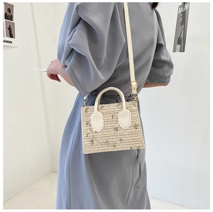 Detail of straw woven tote featuring green floral embroidery and white leather handles