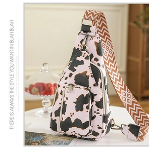 Close-up of cow print sling bag with multi-zipper layers and geometric strap