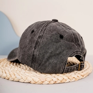 Washed dark grey baseball cap with adjustable metal buckle on a woven straw mat