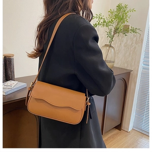 Brown faux leather crossbody bag with wave-edge flap and fringe detail on black blazer