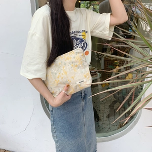 Close-up of beige embroidered floral cosmetic bag held by a model in a minimalist setting