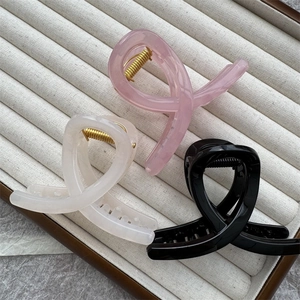 Detailed view of twist-shaped hair claws in pink, cream, and black on a display tray