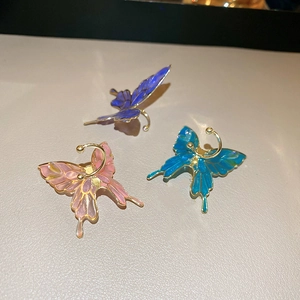 Macro detail of butterfly ear clips in blue, purple, and pink with golden metal frames