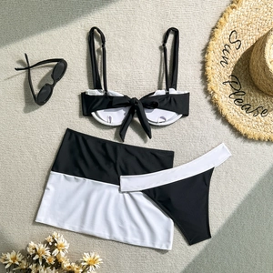 Detailed flat lay of a black and white three-piece bikini set with a bow and skirt