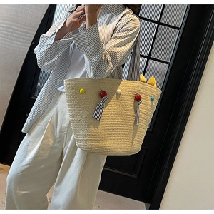 Detailed texture of hand-woven straw tote bag with colorful pompom and ribbon accessories