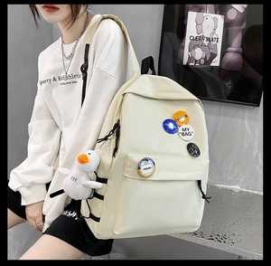 Detail view of cream canvas backpack with colorful badges and a cute duck plush pendant