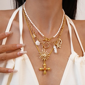 Layered gold necklace featuring freshwater pearls, sun and cross charms on a model