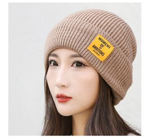 Detail of beige knitted beanie with embroidered yellow text patch for autumn and winter
