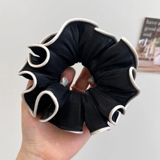 Close-up of black velvet scrunchie with white wavy pleated edges held by hand