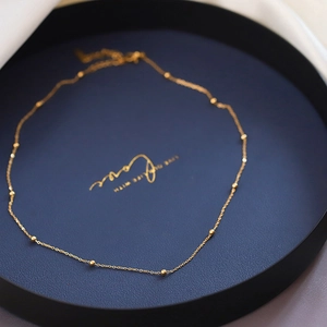 Détail d'un collier doré avec petites billes dans un plateau bleu avec texte décoratif