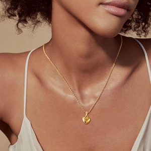 Dettaglio di una collana con pendente a cuore dorato e zircone evil eye su una modella
