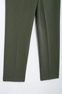 Détail à plat d'un pantalon de costume vert avec pli central marqué et texture coton