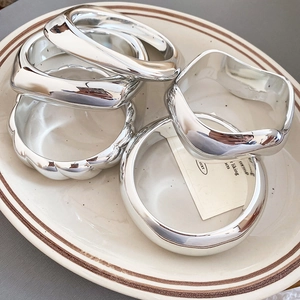 Polished silver geometric bracelets in various shapes shown on a ceramic display