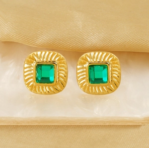 Macro detail of vintage gold square earrings with emerald green zircon on marble