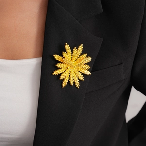 Detail of golden sunburst flower brooch with textured petals on a black blazer lapel