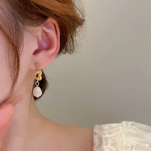 Gros plan de boucles d'oreilles nœud doré avec perle d'eau douce baroque sur un modèle