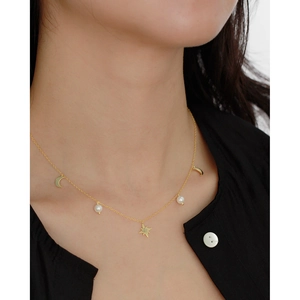 Elegant gold necklace with star, moon pendants and pearls worn on a model's neck