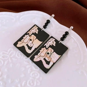Macro shot of vintage rectangular earrings with shell art pattern on white ceramic plate