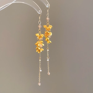 Detail of yellow flower earrings with long tassels and crystal beads on a grey background