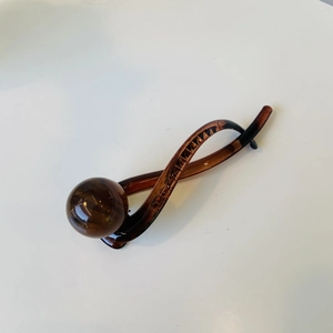 Detail view of a translucent amber twisted hair clip with a round ball decorative element