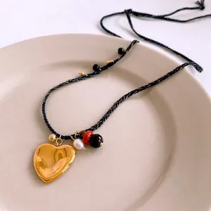 Collier en corde tressée avec pendentif cœur doré et perles d'eau douce sur plateau