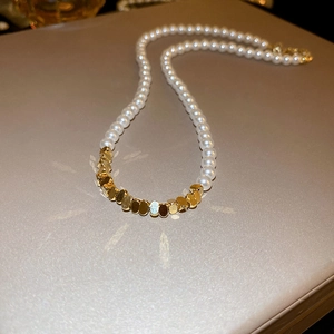 Close-up of irregular gold metal pieces and white pearls on a French vintage necklace