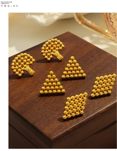 Macro detail of gold-plated geometric earrings with beaded texture on a wooden background