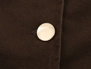 Dettaglio ravvicinato di un bottone dorato lucido su trama di tessuto twill marrone scuro
