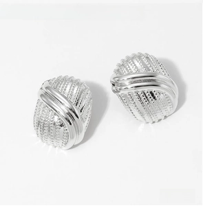 Detailed macro view of silver oval earrings with frosted texture and crossed lines