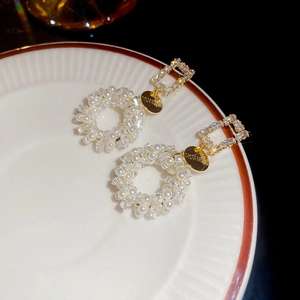 Detail of gold pearl earrings with square zircons and M&S tags on white plate