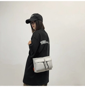 Side view of lightweight gray nylon crossbody bag with dual utility front pockets