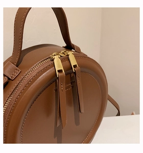 Detailansicht der braunen runden Ledertasche mit Doppelreißverschluss und Griff