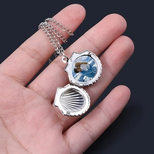 Silver stainless steel shell locket necklace for photos held in hand on blue background