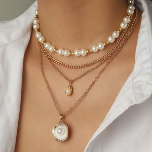 Layered gold necklace featuring starfish, pearls and shell pendants on a white shirt