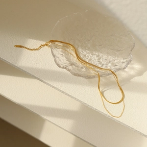 Zweilagige 18K vergoldete Schlangenkette und Ankerkette auf einer Glasschale