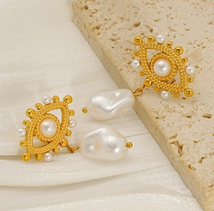 Macro detail of 18K gold-plated Evil Eye earrings with baroque pearls on white silk fabric