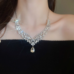 Detail of silver V-shaped necklace with teardrop crystal pendant worn by model on neck