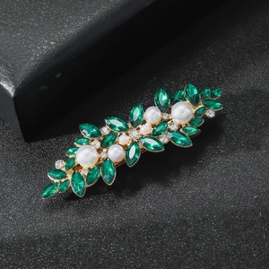Détail d'une pince à cheveux en cristal vert avec perles blanches et base dorée