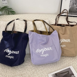 Detailed view of color-block tote bags featuring plaid handles and Bonjour magic print