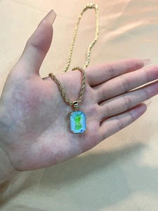 Close-up of rectangular blue and green gradient crystal pendant on a gold twisted chain