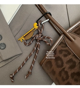 Détail du sac léopard avec nœud tressé, breloque raquette de tennis et porte-clés doré
