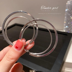 Close-up of double-layered silver geometric hoop earrings with polished metal finish