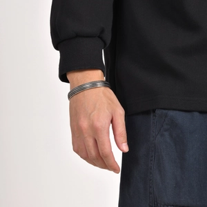 Men's silver twisted rope cuff bracelet shown on model wrist with black sleeve background