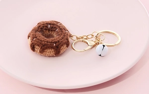 Detailed close-up of brown and beige crochet donut keychain with bell on a pink plate