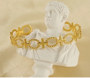 Detail of gold-plated hollow cross and twisted ring open bangle on white statue