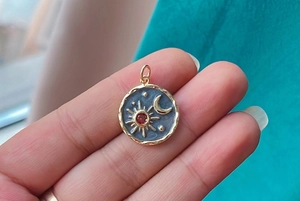 Detail of a gold sun and moon celestial pendant featuring a central red gemstone