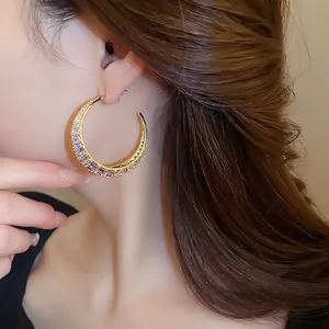 Golden crescent hoop earrings featuring purple zircon stones worn by a model